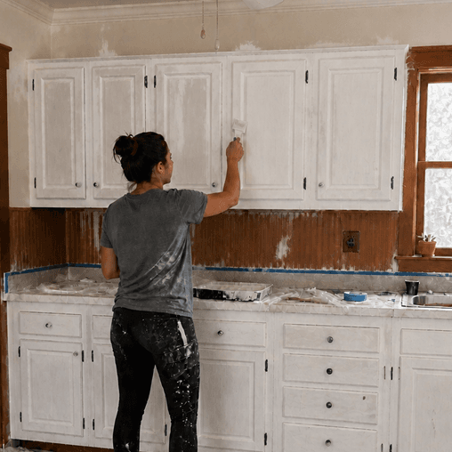 A homeowner painting white kitchen cabinets by hand.