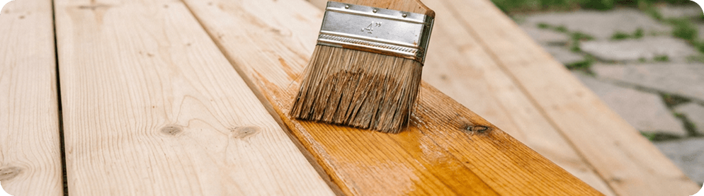 A contractor applying wood stain to a large wood surface.